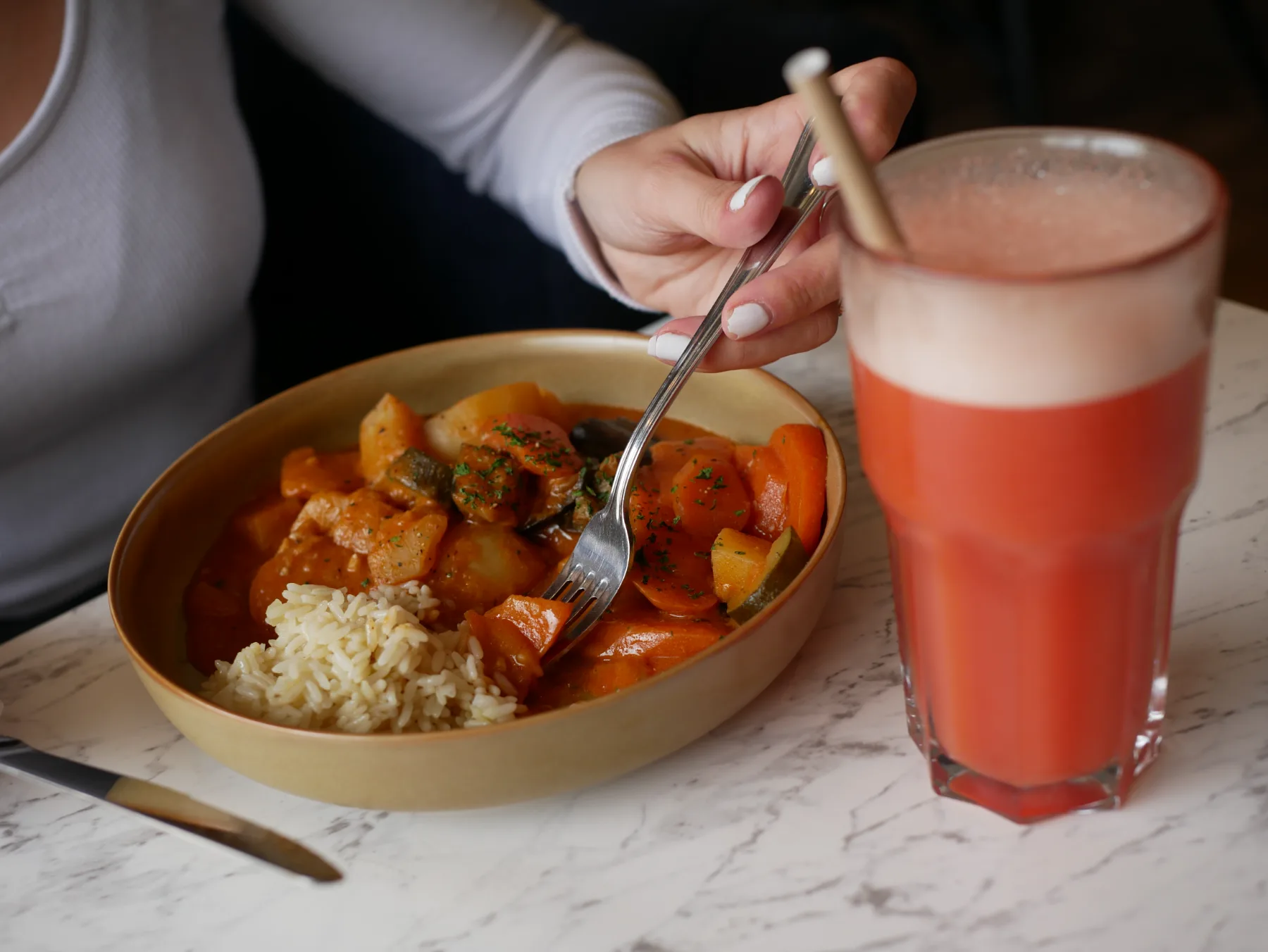 A slow-cooked vegetable dish with rice, served in a bowl with red lemonade on a marble table.
