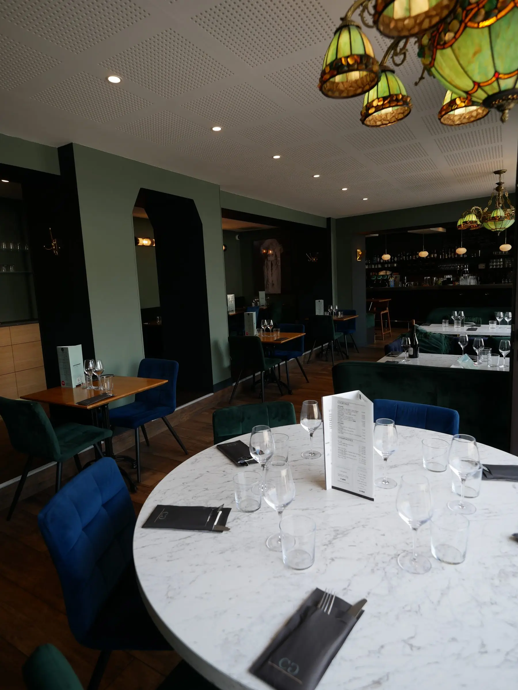 Salle du Café Gourmand : tables de marbre dressées et bar en fond.