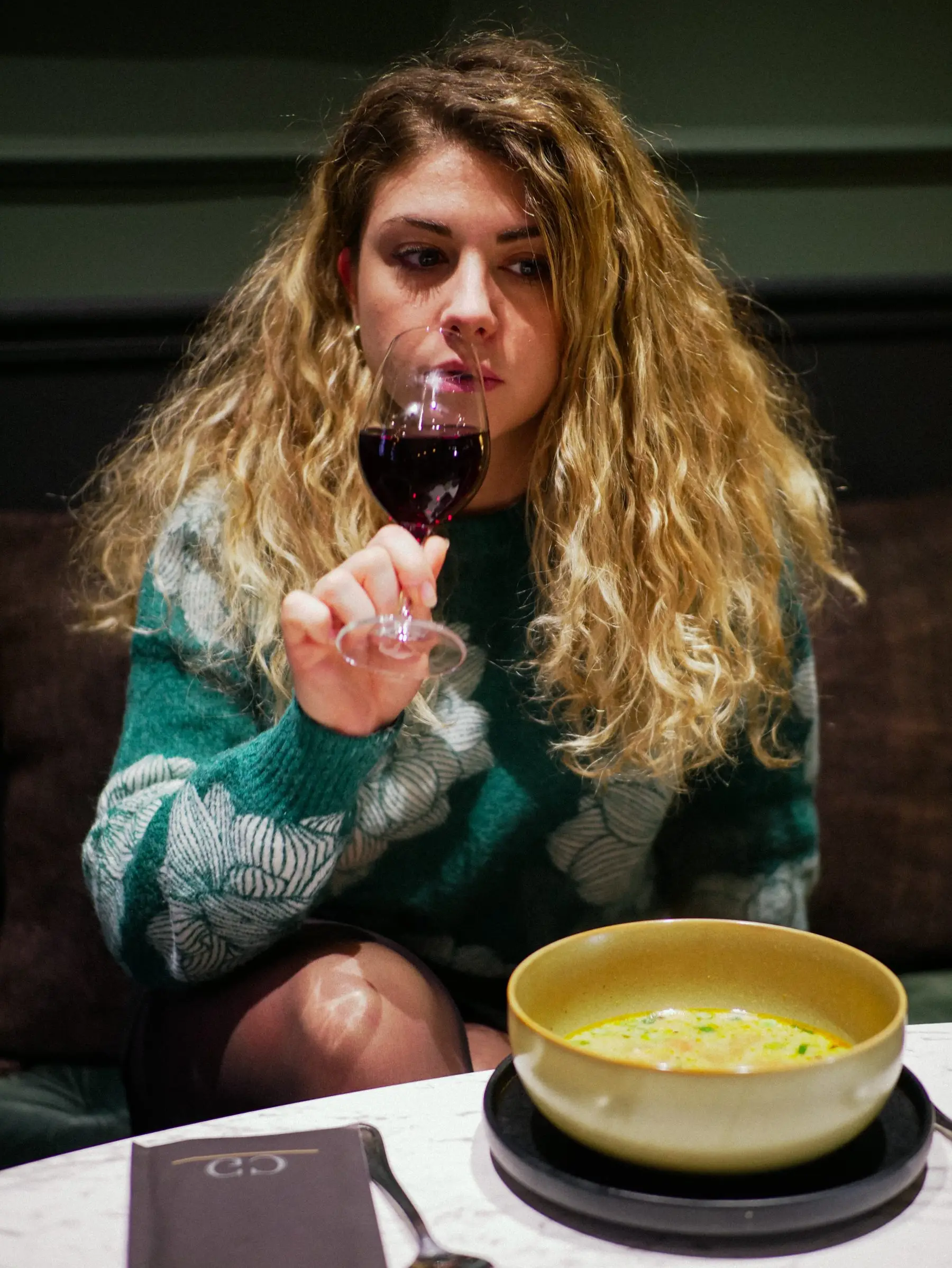 Cliente dégustant un verre de vin rouge devant une soupe, banquette de velours du Café Gourmand.